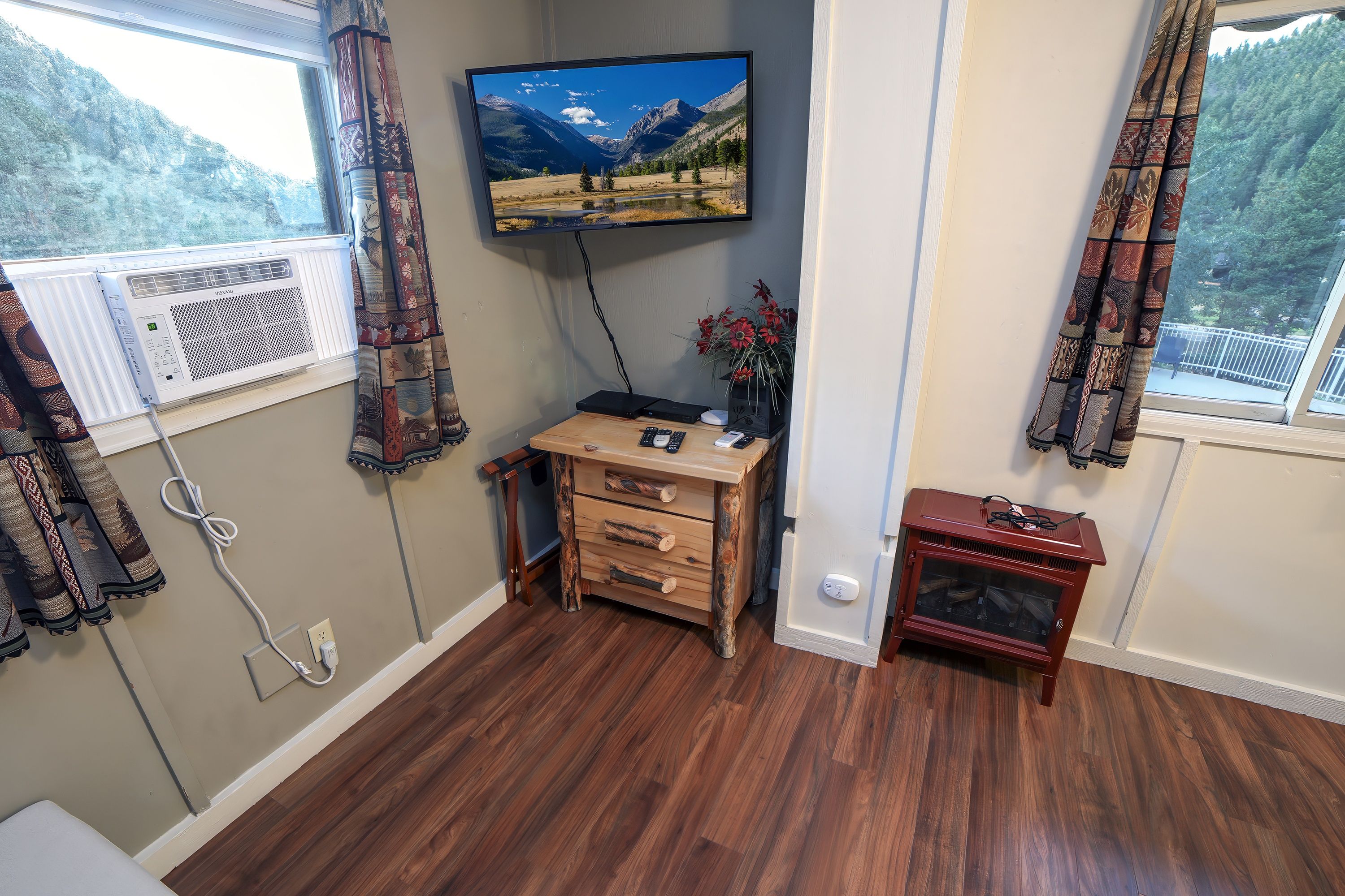 A room with a wooden desk, a television mounted on the wall, a fireplace, and a window with curtains.