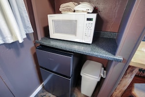 A compact kitchenette with a microwave, a small refrigerator, and a trash bin.