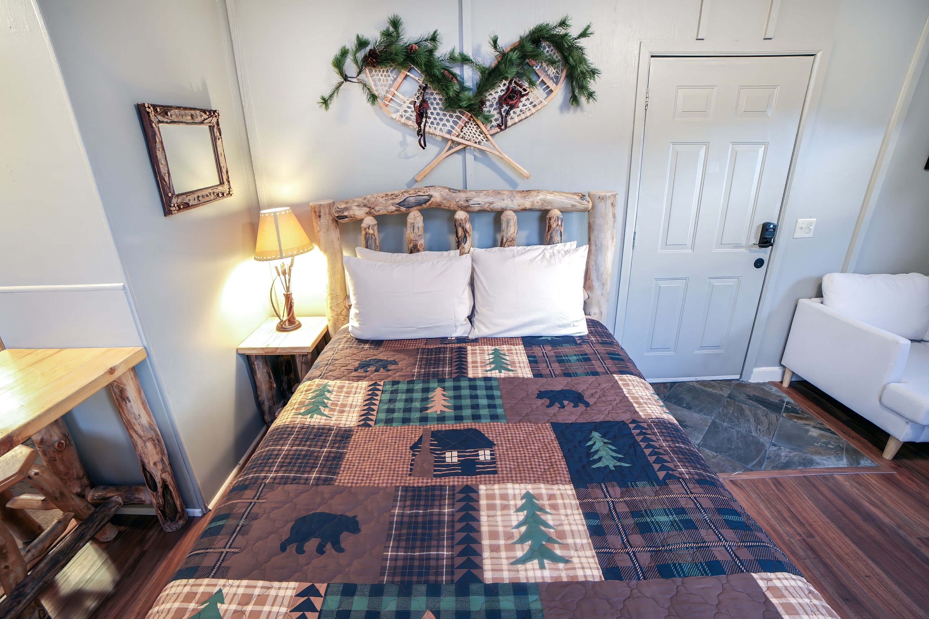 Une chambre à coucher avec une tête de lit en bois, une courtepointe ornée de motifs représentant des animaux et des arbres, une porte blanche et un canapé blanc.