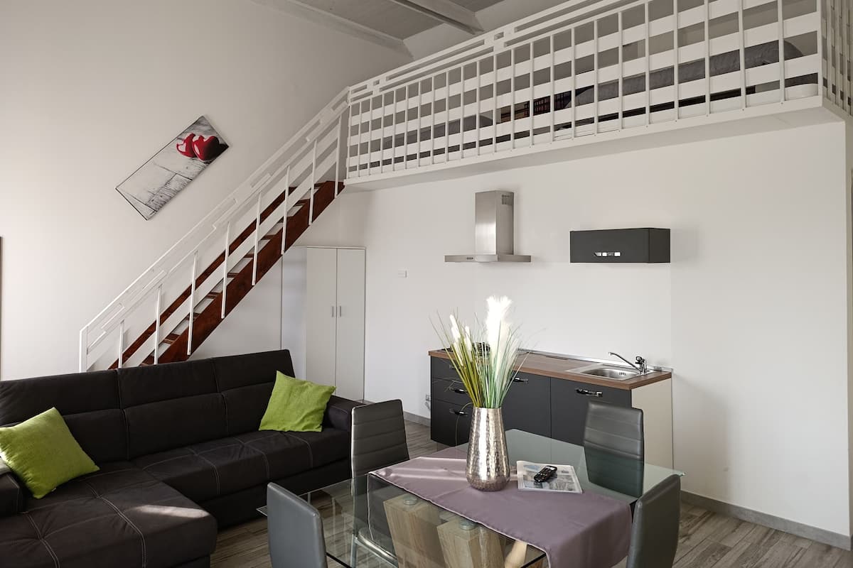 A modern living space with a staircase, a sofa, a glass table, and a kitchen area.