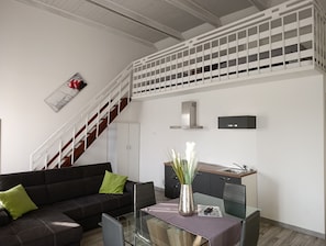 Um espaço de estar moderno com escada, sofá, mesa de vidro e área de cozinha.