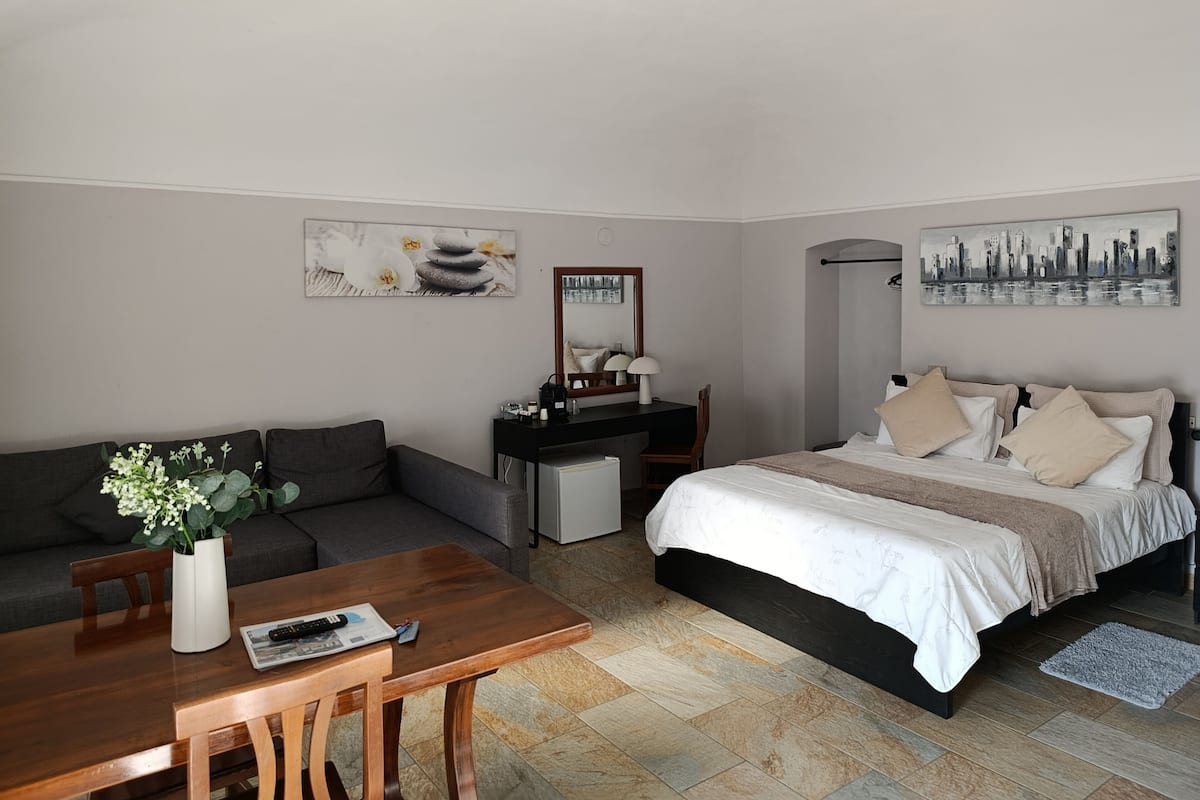 A bedroom with a bed, a desk, a chair, a sofa, and a small table with a vase of flowers.
