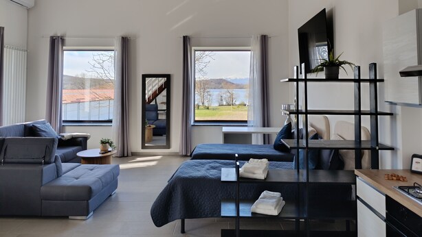 Habitación de hotel moderna con sofá, dos camas, televisor, una planta y vistas al exterior.