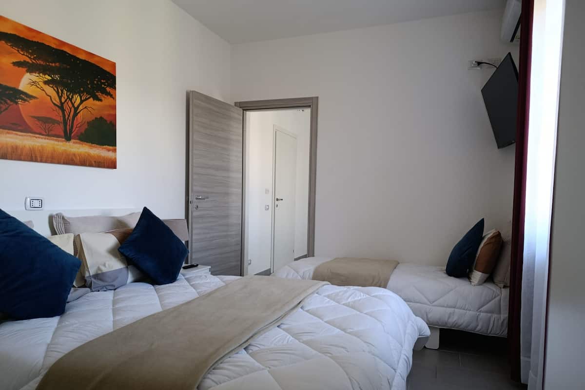 A bedroom with two beds, a door, a painting, and a TV on the wall.
