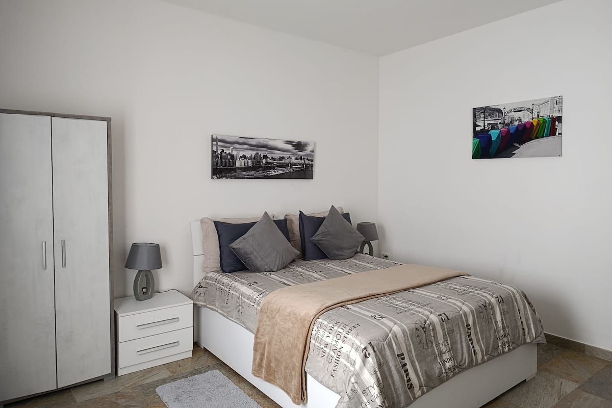 A bedroom with a bed, a wardrobe, a bedside table, a lamp, and two wall-mounted pictures.