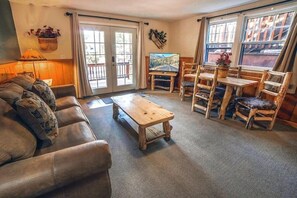A living room with a sofa, a wooden coffee table, a TV, and a dining area with wooden chairs and a table. - Lawn Lane A - #3382 by RedAwning (Estes Park)