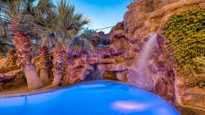A pool with a waterfall and palm trees. - Mollie's Landing 7 Bedroom Home (Hurricane)