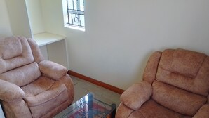Two armchairs and a glass-top coffee table in a room with a tiled floor and a window with bars.
