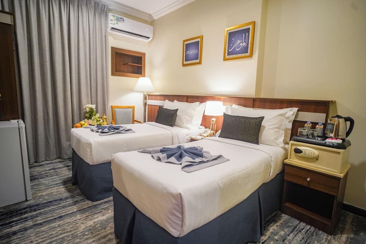 Habitación de hotel con dos camas, un minibar, un escritorio y una ventana con cortinas.