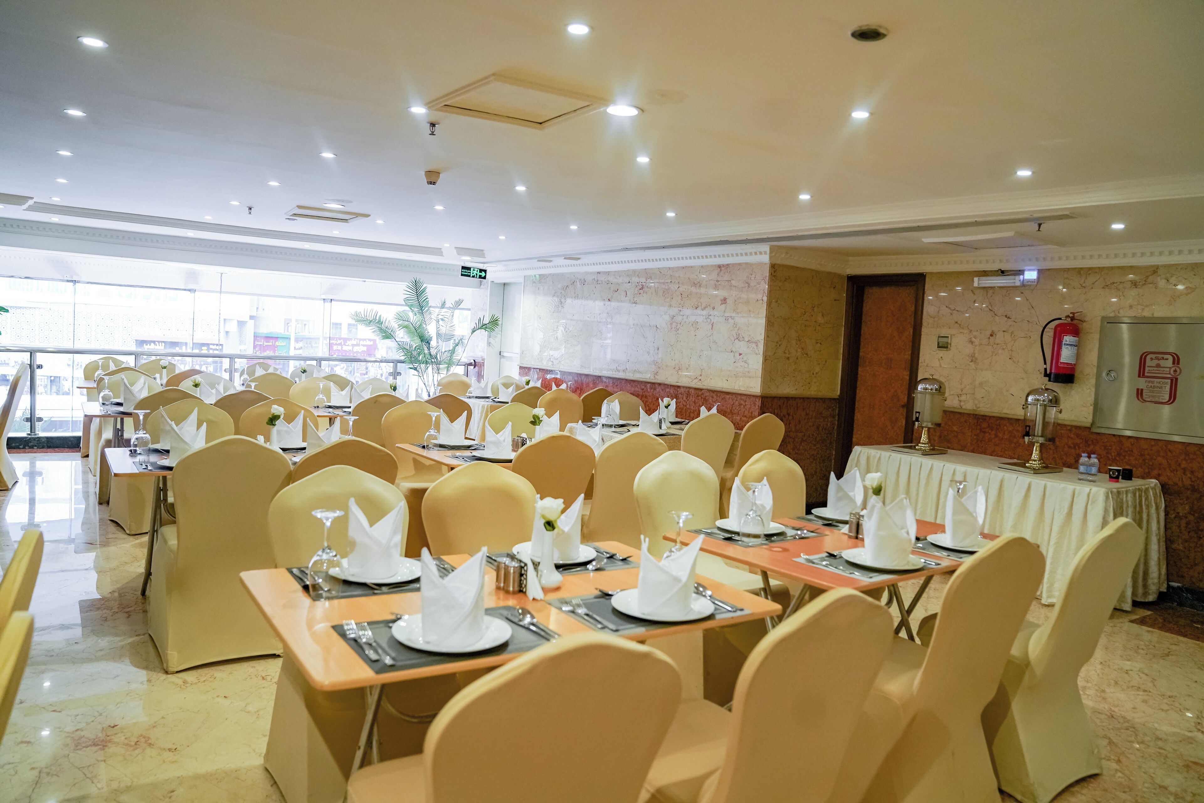 A banquet hall with multiple tables set for dining, equipped with chairs, plates, and cutlery.