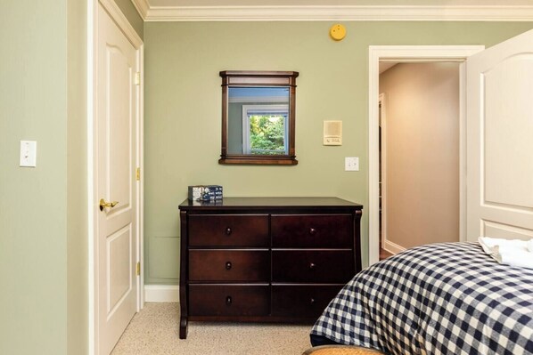 Una camera da letto con un comò in legno scuro, un letto con copriletto a quadretti e una finestra vista sul verde.