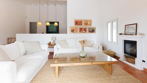 Una sala de estar moderna con un sofá blanco, una mesa de centro de vidrio y una chimenea. Hay cuadros enmarcados en la pared y una lámpara colgante.