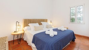 Una cama bien hecha con ropa de cama blanca y azul, un cabecero tejido y dos lámparas de noche.