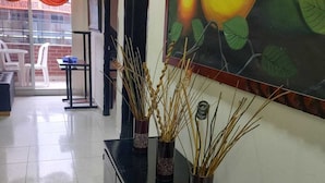 Un couloir doté d’un sol carrelé, une console noire ornée de vases décoratifs et un grand tableau représentant des fruits accroché au mur.