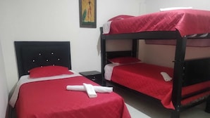 Une chambre avec deux lits superposés, chacun recouvert d’une couverture rouge et agrémenté d’oreillers blancs. Une petite table et une chaise se trouvent à côté des lits.