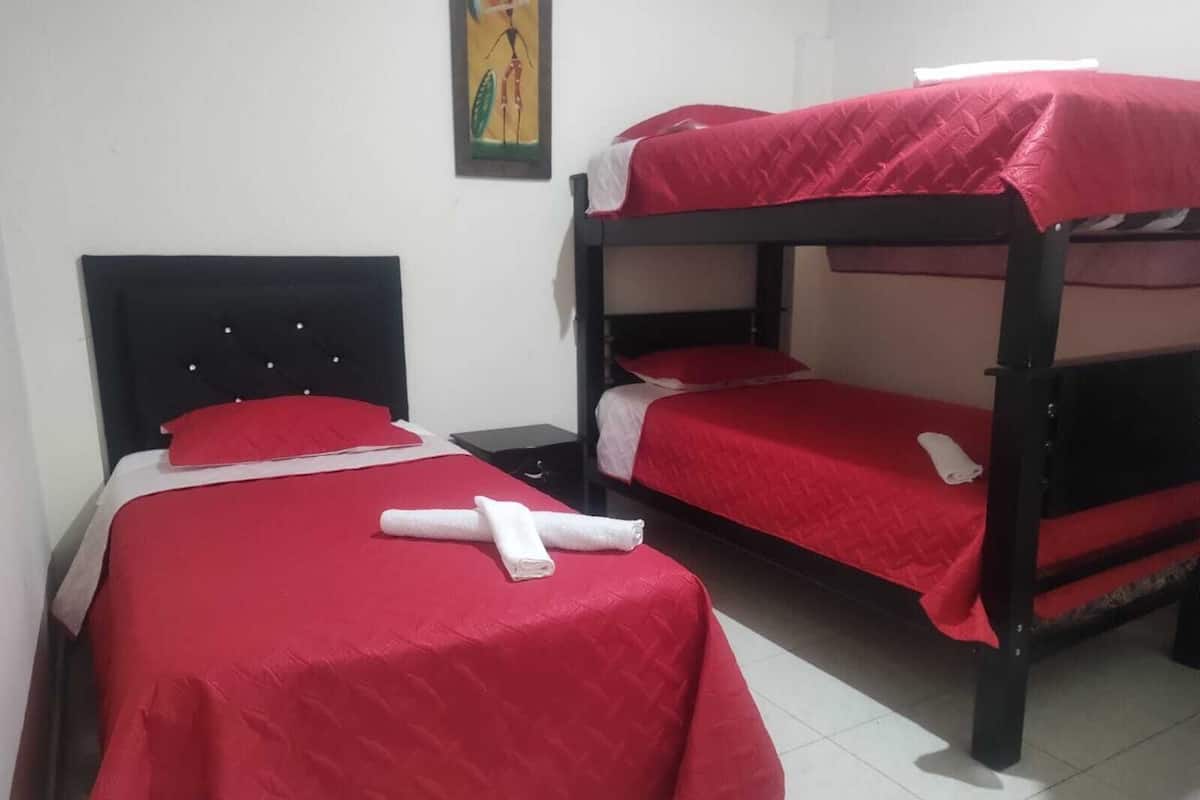 A room with two bunk beds, each with a red bedspread and white pillows. There is a small table and a chair next to the beds.