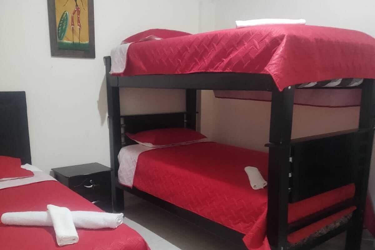 A bunk bed room with red bedding, a small table, and a painting on the wall.