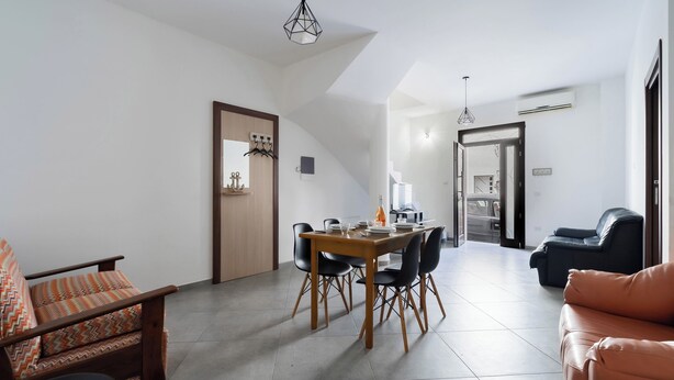 Un coin repas comprenant une table et des chaises en bois, un canapé et un fauteuil agrémenté d’un coussin à motifs.