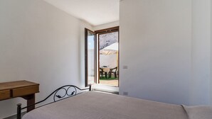 Une chambre à coucher avec un lit, un bureau en bois et une fenêtre donnant sur une terrasse extérieure.