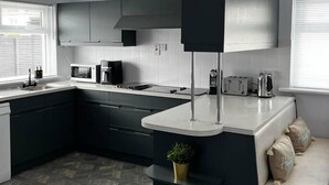 Una cocina moderna con armarios oscuros, una encimera blanca, microondas, cafetera y tostadora.