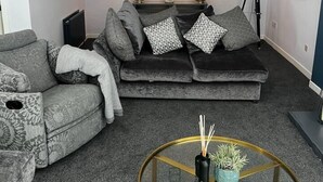 Una sala de estar moderna con un sofá gris estampado, un sofá negro con cojines estampados y una pequeña mesa redonda de centro con una planta.