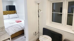 A hotel room with a bed, a bedside table, a lamp, a window, and a radiator. - Stunning Well Decorated 1bed Apartment in Dartford (Dartford)