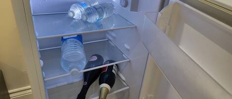 A refrigerator with water bottles and a wine bottle inside.