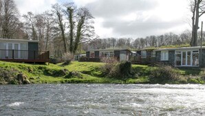 Vista a la orilla del río con varias casas móviles, cada una con terraza cercada y un pequeño porche.