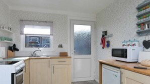 Cocina compacta con lavabo, estufa y microondas. Hay una ventana sobre el lavabo y una puerta con vidrio esmerilado.