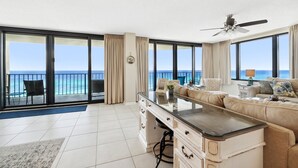 A spacious living room with a large window overlooking the ocean, a ceiling fan, and a sofa with a coffee table. - SURROUNDING VIEWS OF GULF!! BEAUTIFUL 2/2 AVAILABLE NOW!! (Panama City)