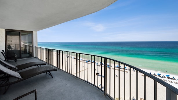 A balcony with two lounge chairs, a glass door leading to a beach view, and a railing overlooking the ocean. - SURROUNDING VIEWS OF GULF!! BEAUTIFUL 2/2 AVAILABLE NOW!! (Panama City)