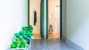 A hallway with a tiled floor, a potted plant, a hanging coat, and a door leading to a room. - Ninfea Apartments by Wonderful Italy - Teal (Lezzeno)