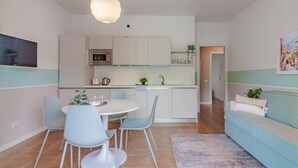 A modern kitchen with white cabinets, a dining area with a round table and blue chairs, and a light blue sofa in a living area. - Ninfea Apartments by Wonderful Italy - Teal (Lezzeno)