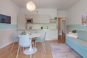 Een moderne keuken met witte kasten, een eethoek met een ronde tafel en blauwe stoelen, en een lichtblauwe bank in een woonkamer.