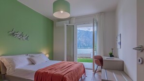 Quarto com cama, escrivaninha, cadeira e vista para um lago e montanhas.