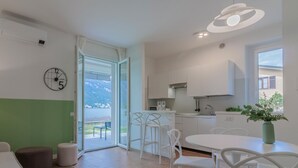 Cozinha moderna com armários brancos, área de jantar com cadeiras brancas e uma grande janela com vista para uma paisagem montanhosa.