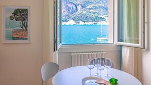 A dining area with a table set for four, a framed picture of a coastal scene, and a view of the sea and mountains through a window.