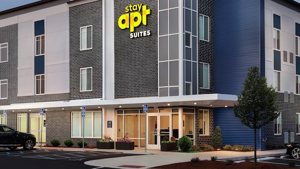 A modern hotel with a 'Stay Apt Suites' sign, featuring a brick facade, large windows, and a parking lot. - stayAPT Suites Auburn (Auburn)