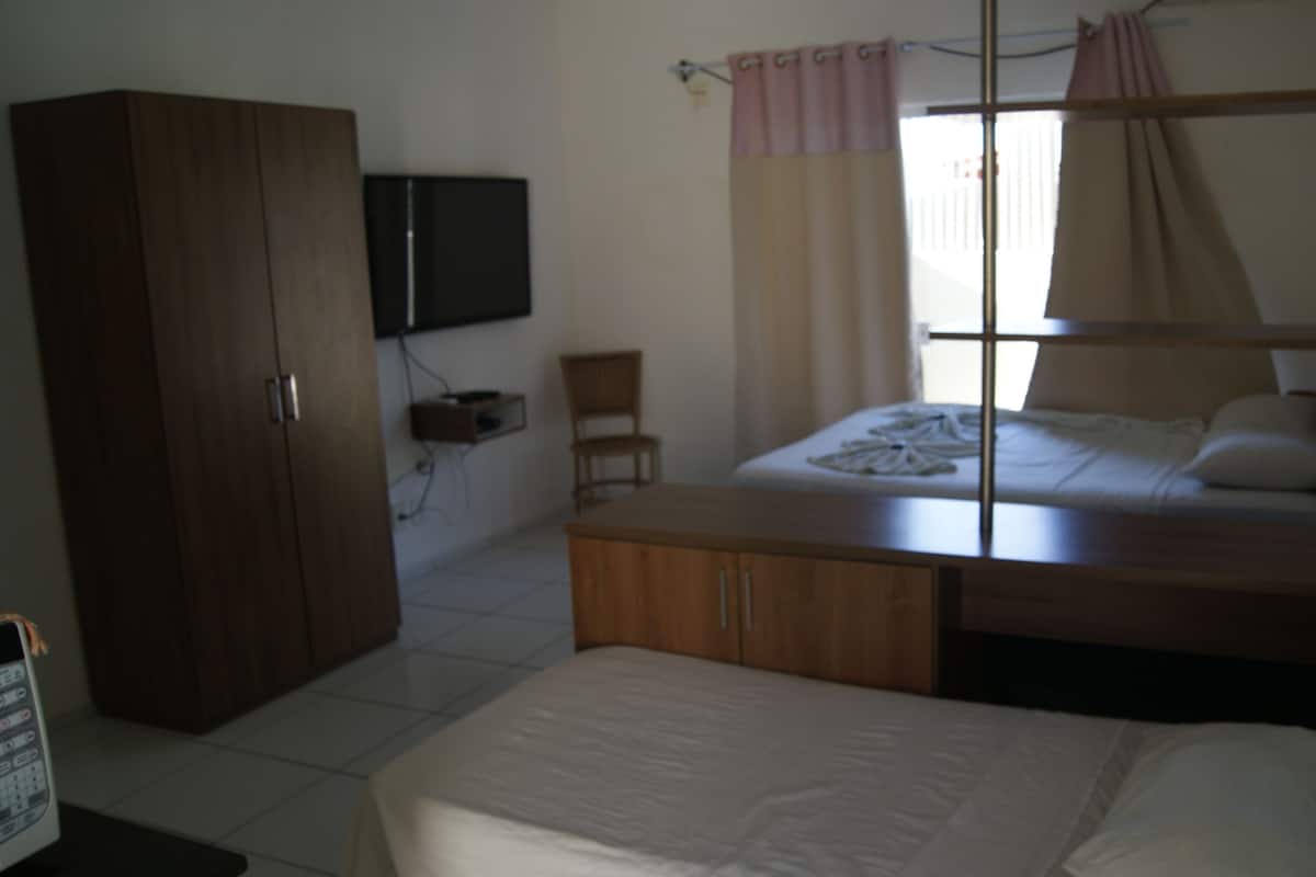 A bedroom with a bed, a wardrobe, a television, and a window with curtains.