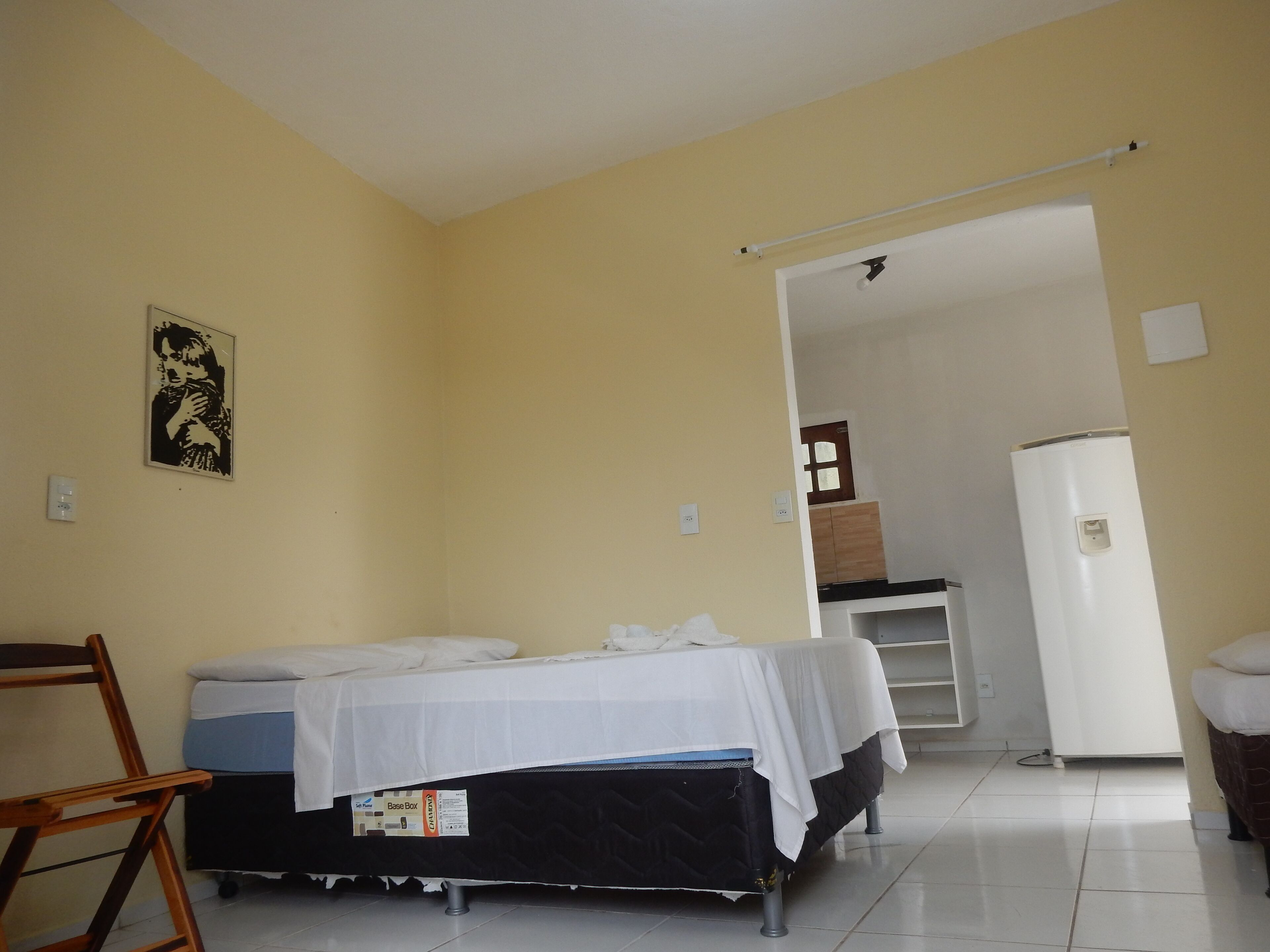 A small, simple room with a bed, a desk, and a refrigerator.