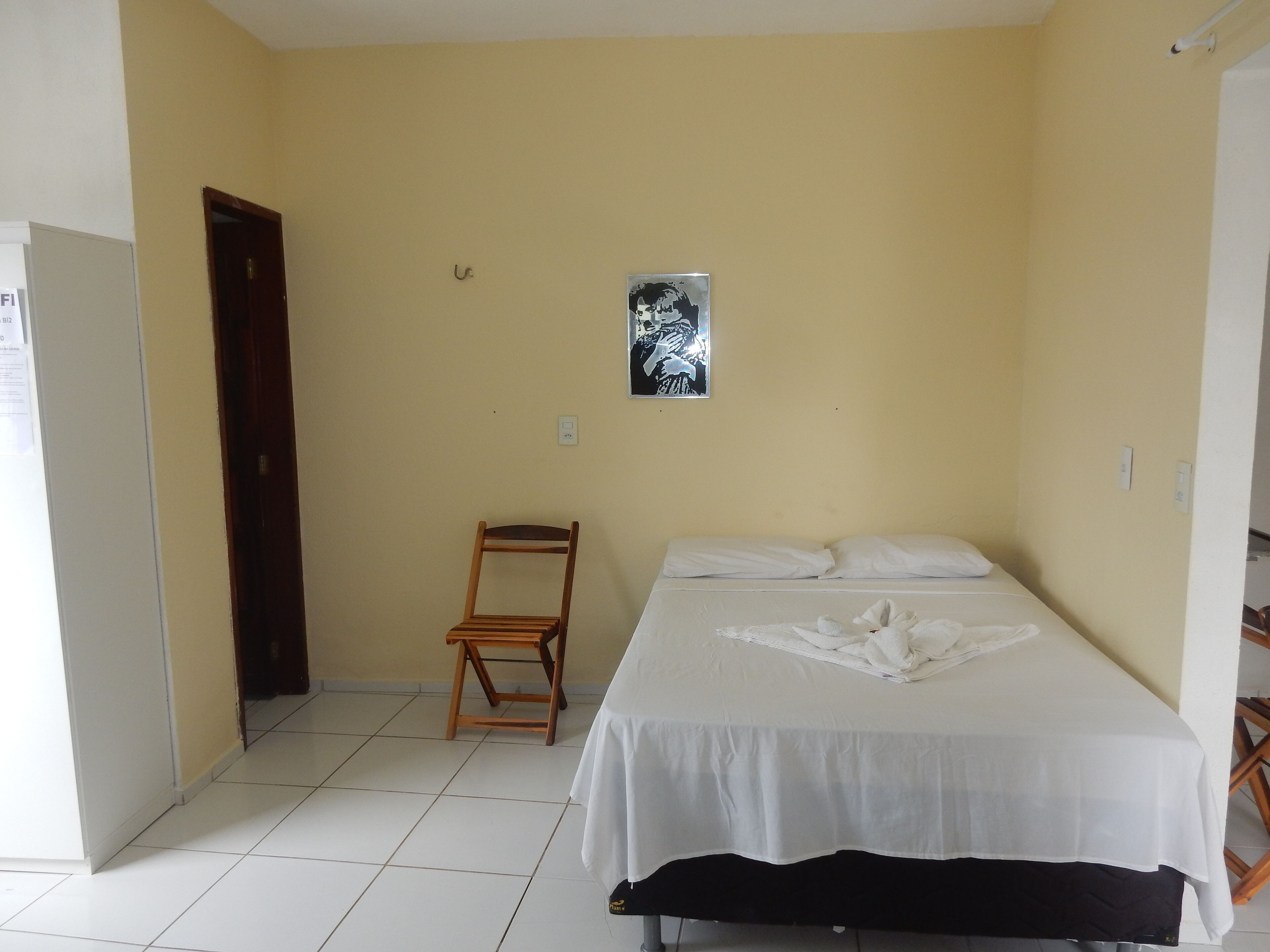 A small, clean room with a single bed, a wooden chair, and a door.