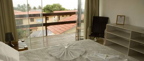 Habitación de hotel con cama, una silla, un escritorio y vista a edificios a través de una ventana.