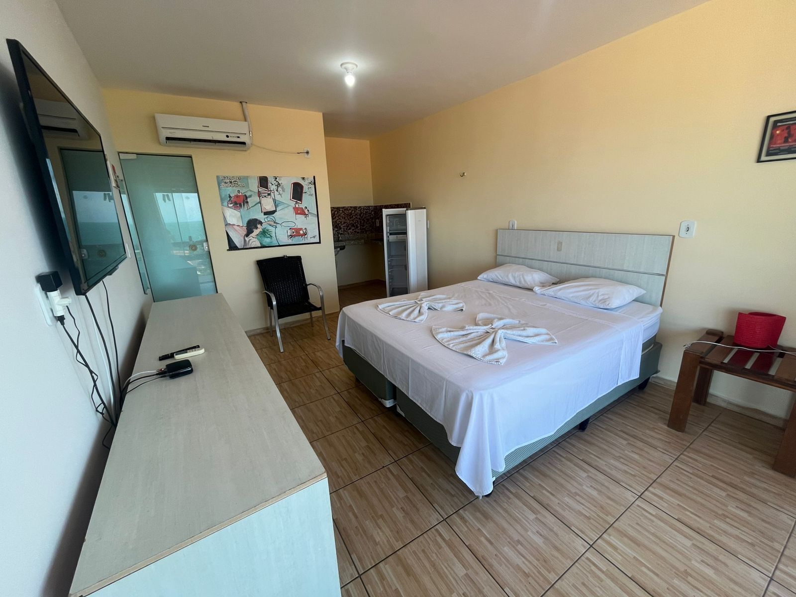 A hotel room with a bed, a desk, a chair, an air conditioner, and a television.