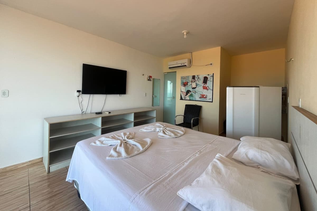 A hotel room with a bed, a TV mounted on the wall, a desk with a chair, and a refrigerator.