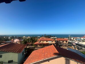 Zona residencial costeira com telhados de cerâmica avermelhada, painéis solares e vista clara para o mar.