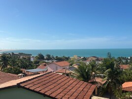 Zona residencial costera con techos de tejas terracota, palmeras y vista al mar y un puente distante.