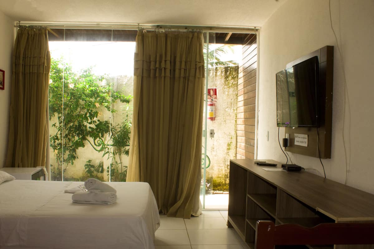 A hotel room with a bed, a TV mounted on the wall, and a balcony with curtains.