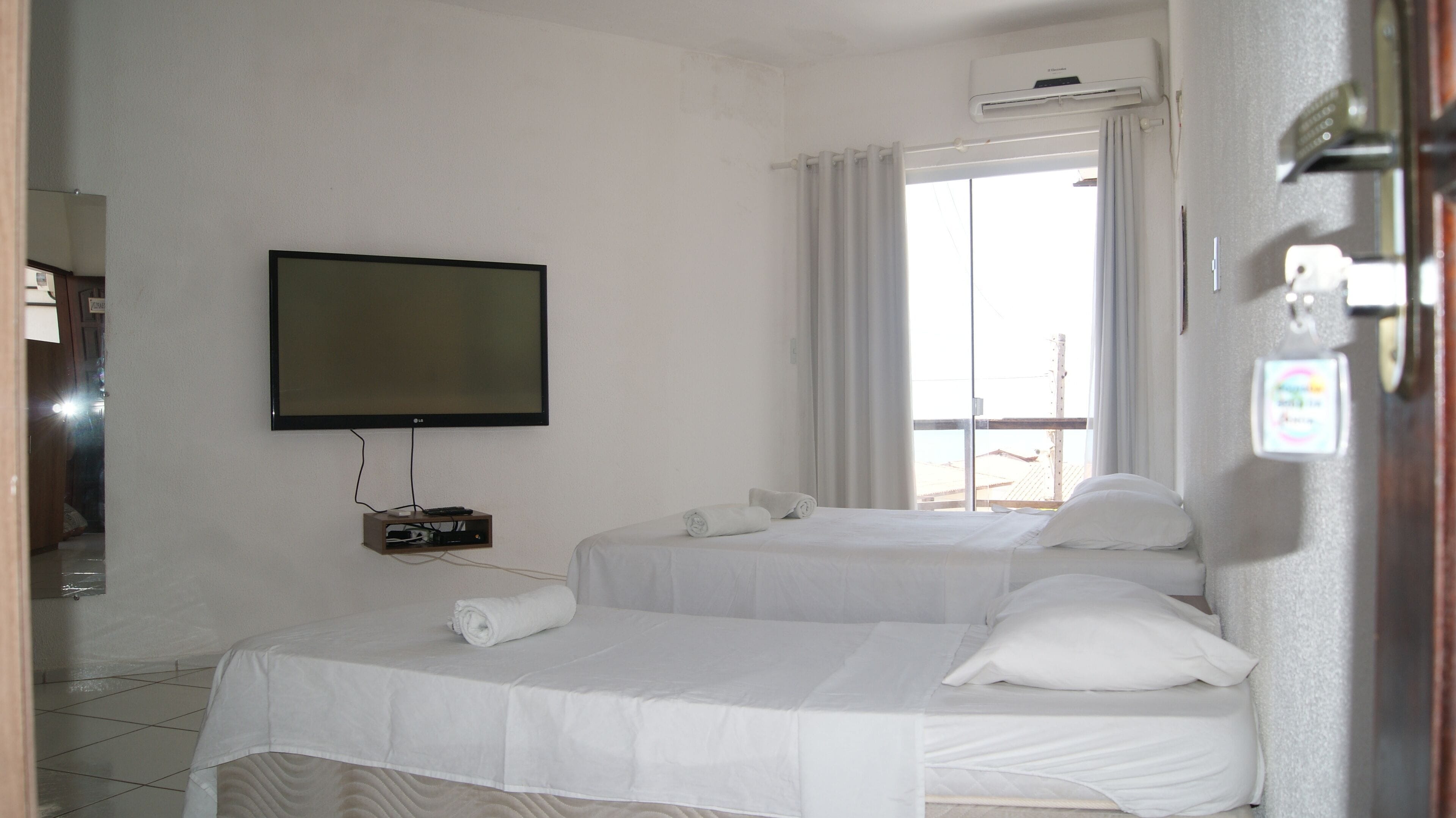 A hotel room with two beds, a TV, and an air conditioning unit.