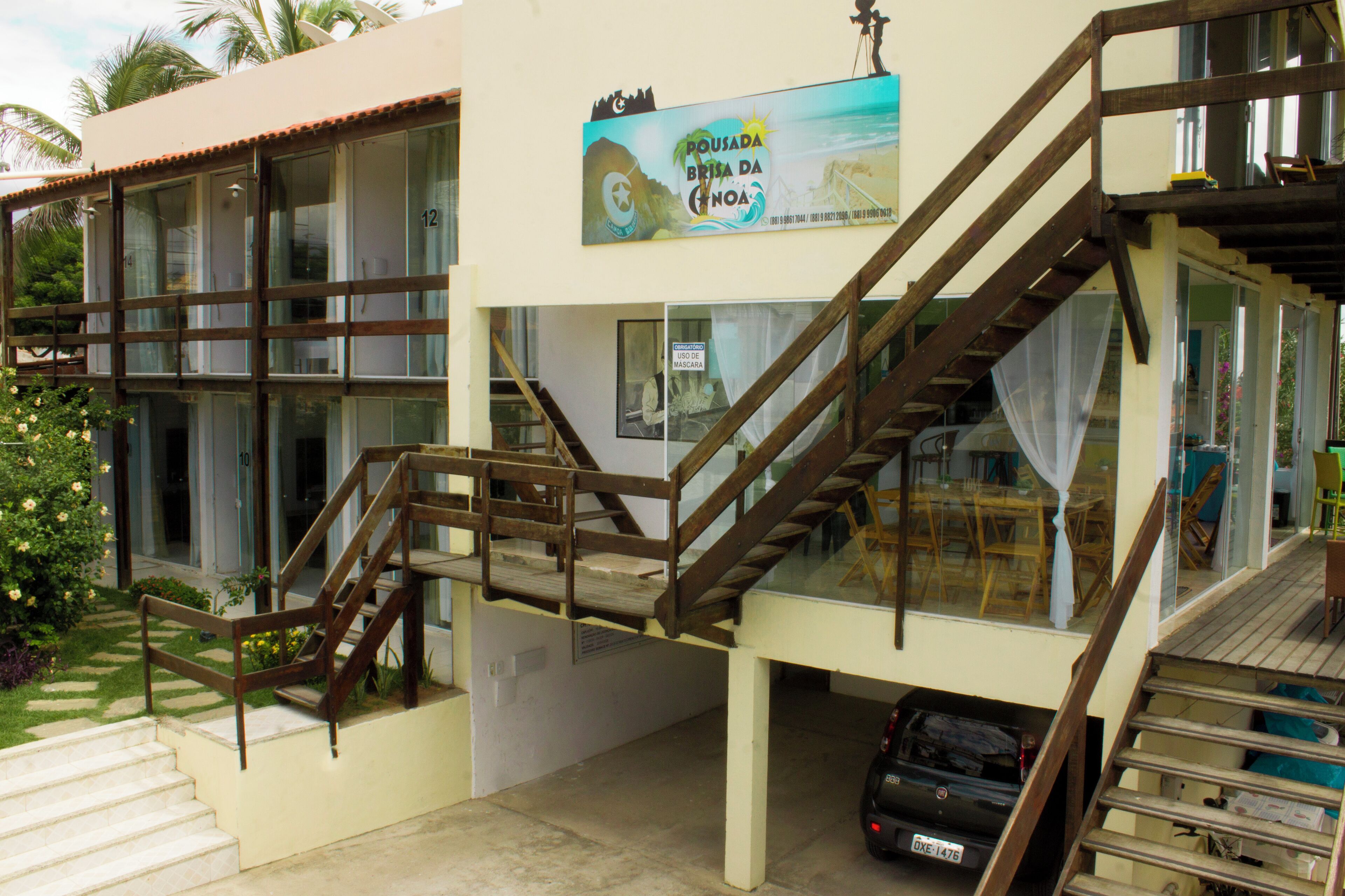 A building with a staircase leading to a balcony, a sign advertising a local event, and a parked car.