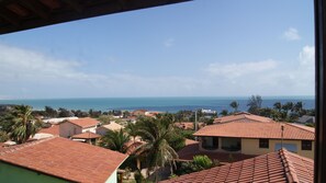 Área residencial costeira com casas de telhado vermelho, palmeiras e vista para o oceano.